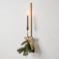 a candle is hanging on the wall next to a christmas tree branch with a bow