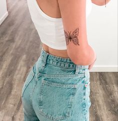 a woman with a butterfly tattoo on her arm and back, standing in front of a mirror