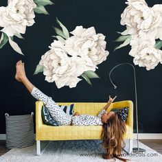 a woman laying on top of a yellow couch in front of a flower wall mural