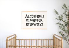 a baby crib in front of a white wall with black letters on it and a potted plant next to the crib