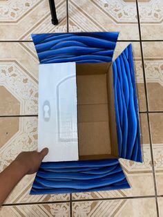 an open box on the floor with blue cloth covering it and a hand reaching out