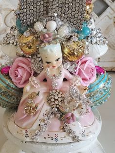 a small figurine sitting on top of a white vase filled with lots of flowers