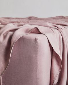 a bed with pink sheets on top of it and a white wall in the background