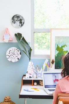 a woman sitting at a desk in front of a laptop computer with a plant on top of it