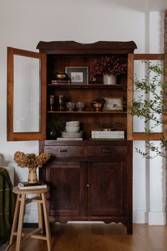 a wooden cabinet sitting in the middle of a living room next to a chair and potted plant