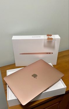 an apple laptop sitting on top of a white box next to a pink macbook pro