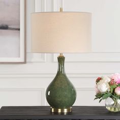 a green vase with flowers sitting on a table next to a lamp