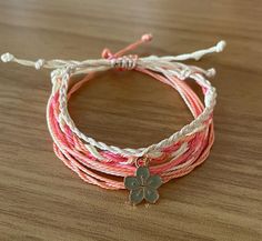 three bracelets with flower charms on them sitting on a table together, one is pink and the other is white