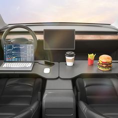 the interior of a car with a laptop, hamburger and fries on it's desk