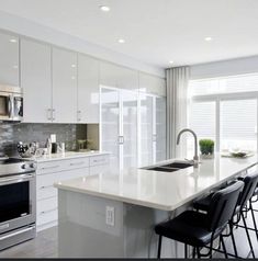 a large kitchen with white cabinets and stainless steel appliances, along with black bar stools