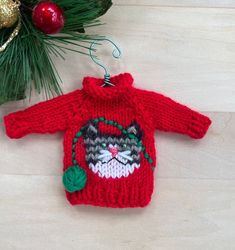 a knitted christmas sweater ornament hanging from a tree branch with ornaments around it