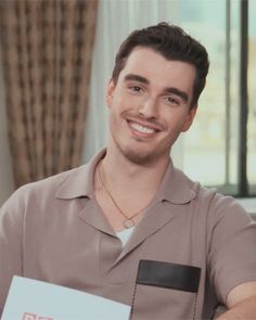 a man is smiling while holding a sign in front of his face and wearing a brown shirt