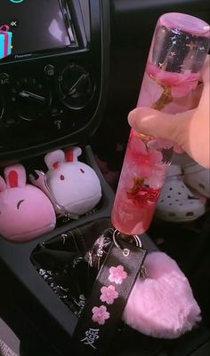 a person is holding a pink liquid in a car with bunny ears on the dashboard