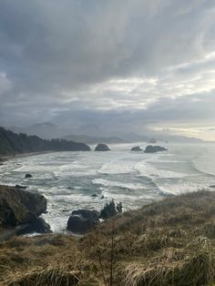 an ocean view with waves crashing on the shore and mountains in the distance under a cloudy sky