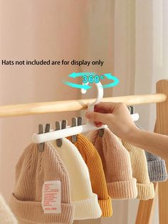 a person is holding three hats on a rack and pointing to it with their finger