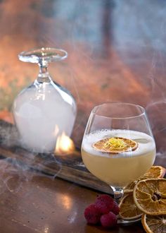 a glass filled with liquid sitting on top of a table next to sliced oranges and raspberries