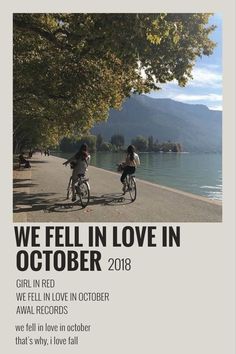 two people riding bikes on the side of a road next to a lake and trees