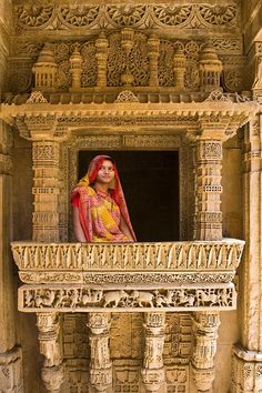 a woman standing on top of a balcony next to stone pillars with carvings around her