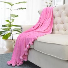 a white couch with a pink blanket on it and a potted plant in the background