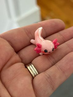 a tiny pink toy fish sitting on top of someone's hand