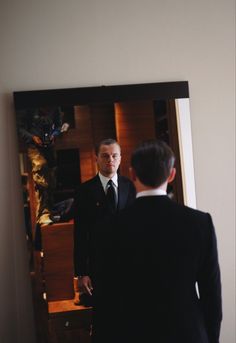 a man standing in front of a mirror wearing a suit and looking at his reflection