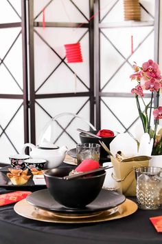 the table is set with black and gold plates, silverware, and pink flowers