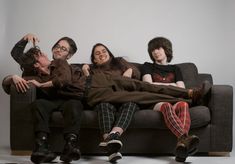 three people sitting on a couch with their arms around each other and one person laying down