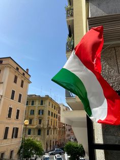 an italian flag is flying in front of a building with cars parked on the street