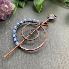 a brooch with blue glass beads and a copper spiral pin on a gray surface