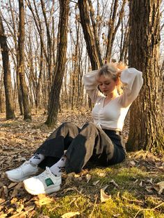 a woman sitting on the ground next to a tree with her head in her hands