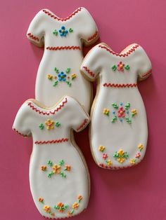 three decorated cookies are sitting on a pink surface