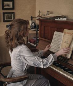 a woman sitting at a piano with an old book in her lap and hands on the keyboard