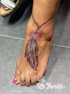 a woman's foot with a tattoo on it and a feather charm hanging from the ankle