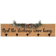 a wooden sign that says and the stockings were hung on hooks with pine cones hanging from them