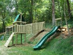 a wooden play set in the woods with a green slide