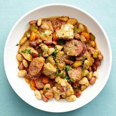 a white bowl filled with beans and meat on top of a blue tablecloth next to a fork