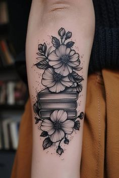 a woman's arm with flowers and books tattoo on the left side of her arm