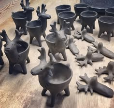 many clay animals are sitting on the floor next to cups and bowls, all in different shapes and sizes