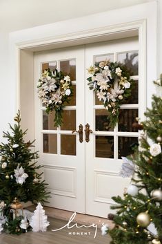 two christmas wreaths on the front door of a house with trees and presents around them