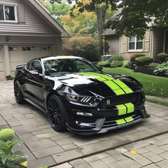 a black mustang with neon green stripes parked in front of a house on a driveway