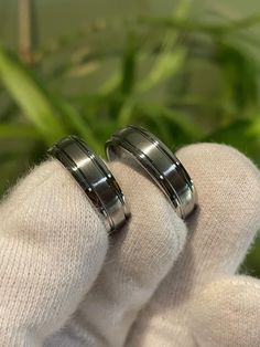 two men's wedding rings sitting on top of each other in front of a plant