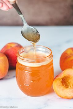 a person is spooning honey into a jar full of peaches and some apples