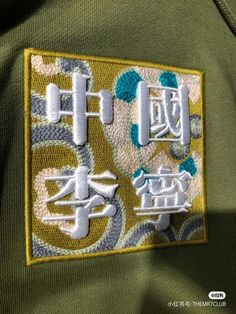 an embroidered patch on the back of a green jacket with chinese writing and symbols in white