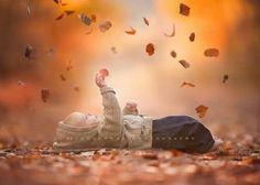 a young boy laying on the ground with his hands up in the air and falling leaves