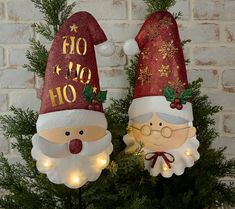 two christmas decorations on top of a tree in front of a brick wall with lights