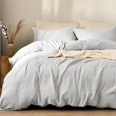 an unmade bed with white sheets and pillows on it, next to a plant