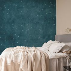 a bed with white sheets and pillows in front of a blue star - patterned wall