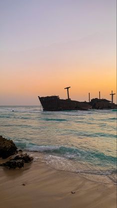 an old ship sitting on top of the ocean next to a sandy beach at sunset