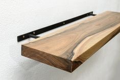 a wooden shelf with black metal brackets on the top and bottom, against a white wall