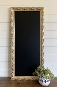 there is a potted plant on the table next to a blackboard with gold trim